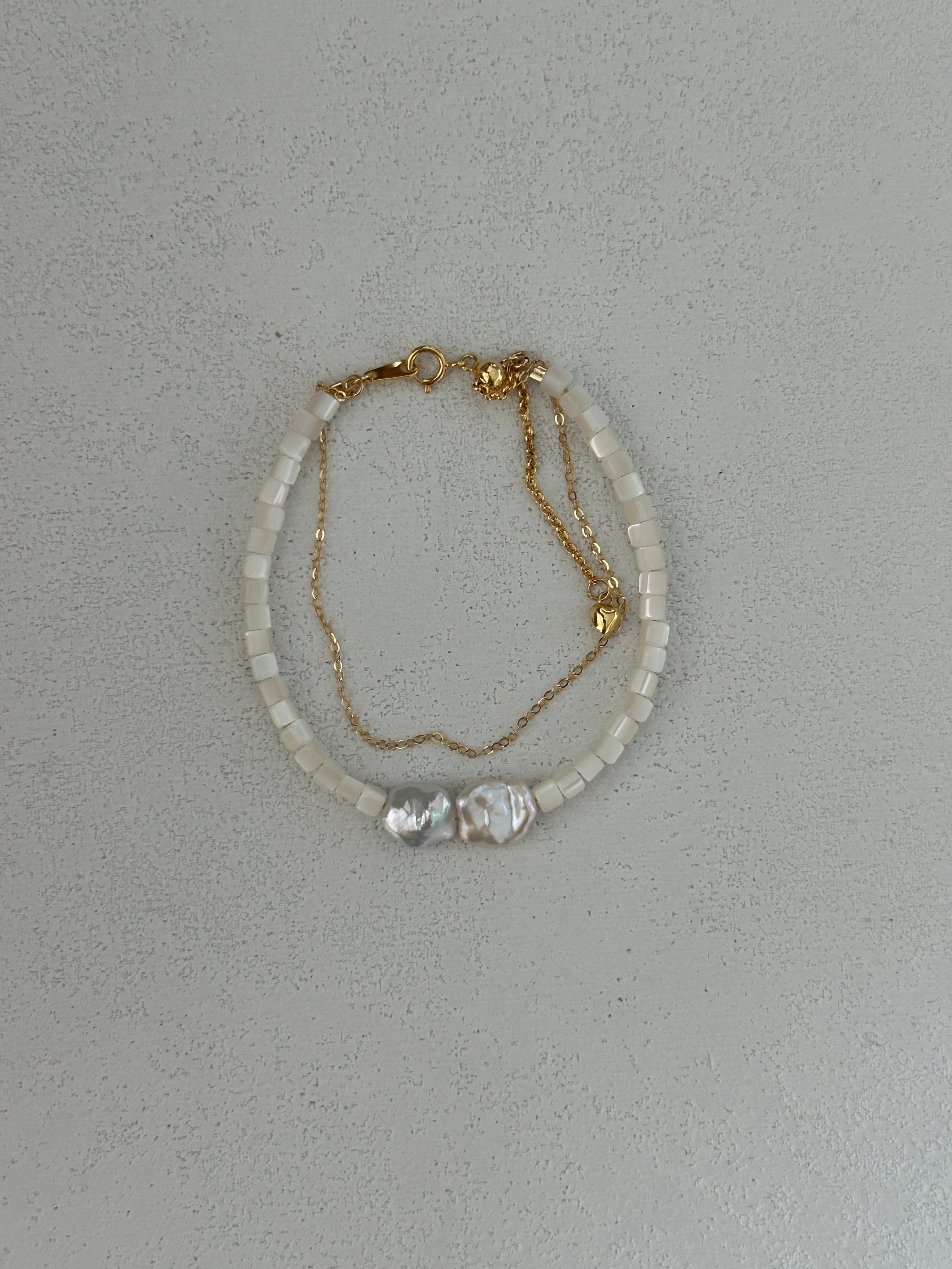 A two-layered pearl bead bracelet with gold plating on a silver chain, featuring a single large pearl at the center.