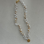 A keshi pearl necklace with gold plating and small gold accents, displayed on a beige surface.