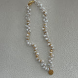 A keshi pearl necklace with gold plating and small gold accents, displayed on a beige surface.