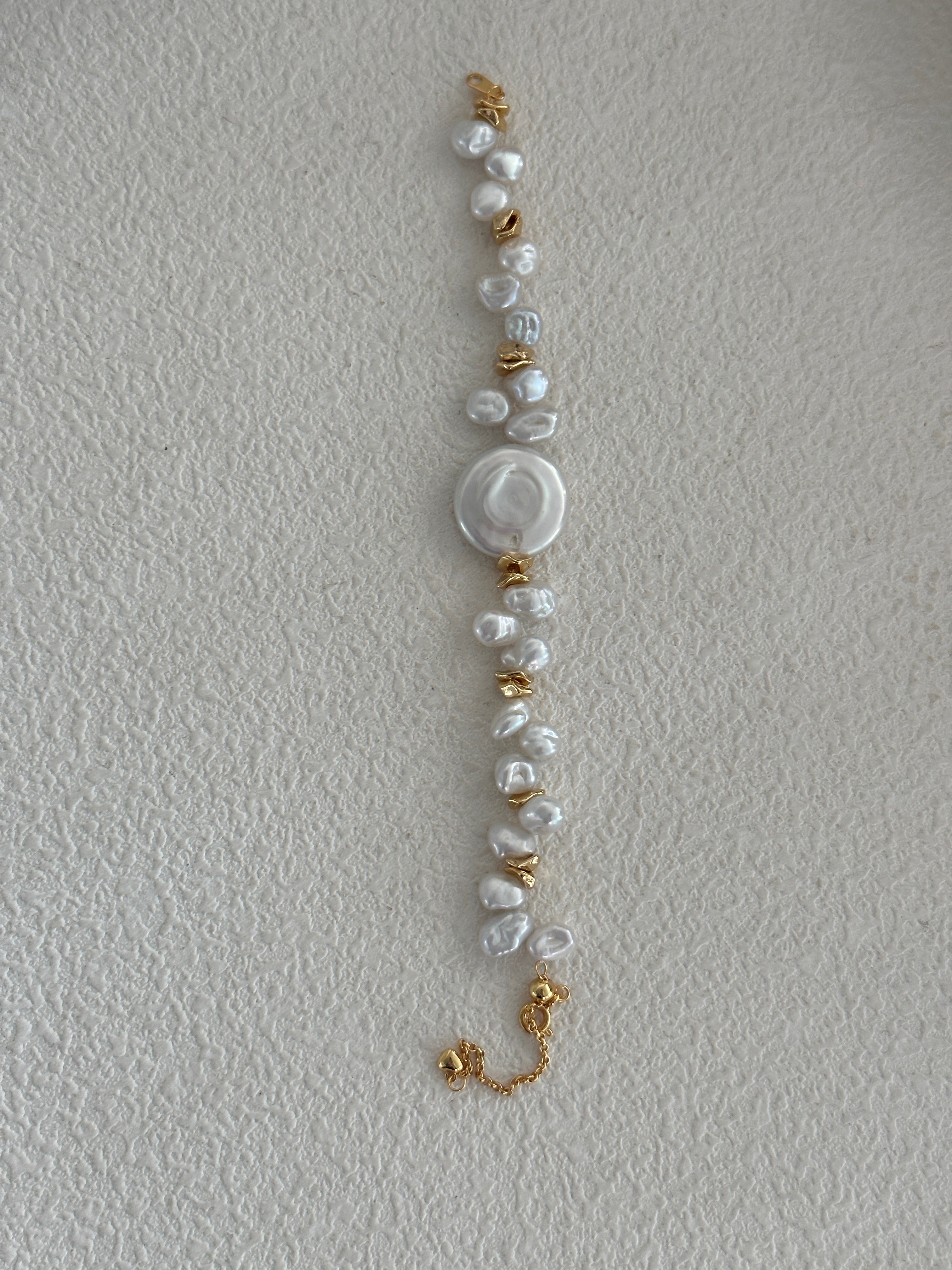 A bracelet with a combination of round pearls and gold-colored accents on a pale background.