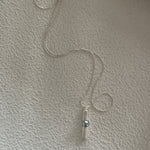 A silver pendant necklace with a keshi pearl dangle, displayed against a textured wall.