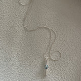 A silver pendant necklace with a keshi pearl dangle, displayed against a textured wall.