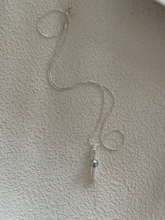 A silver pendant necklace with a keshi pearl dangle, displayed against a textured wall.