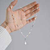 Hand holding a delicate necklace with pearls against a gray background