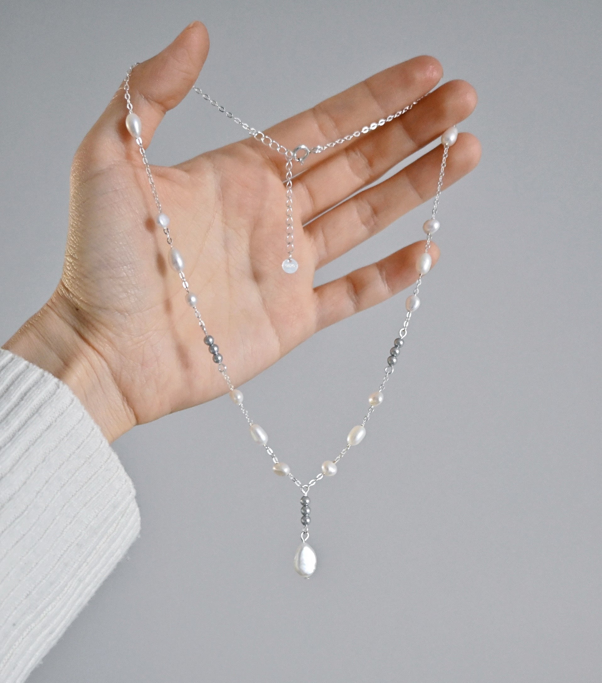 Hand holding a delicate necklace with pearls against a gray background