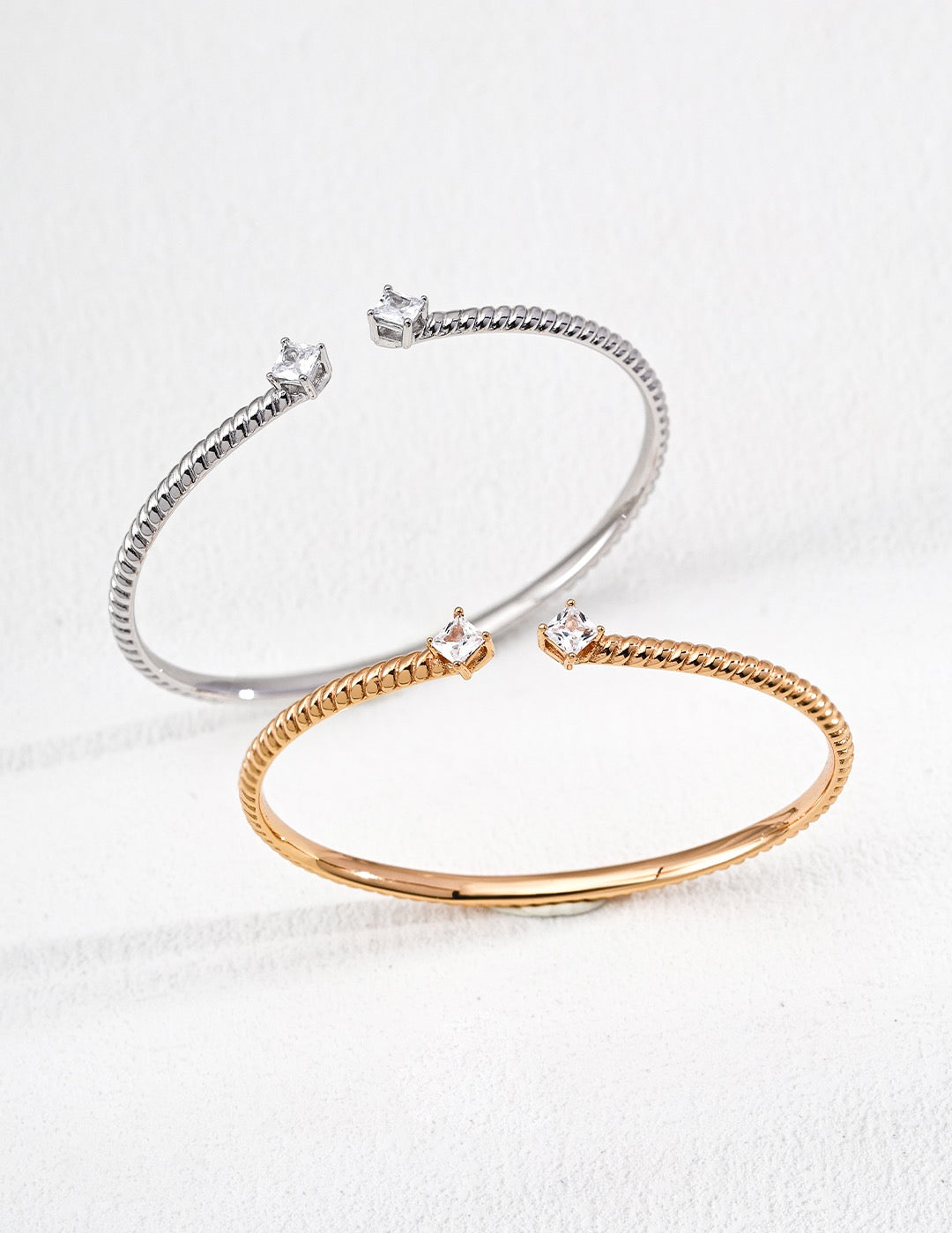 Two bracelets, one silver and one rose gold, on a light gray background