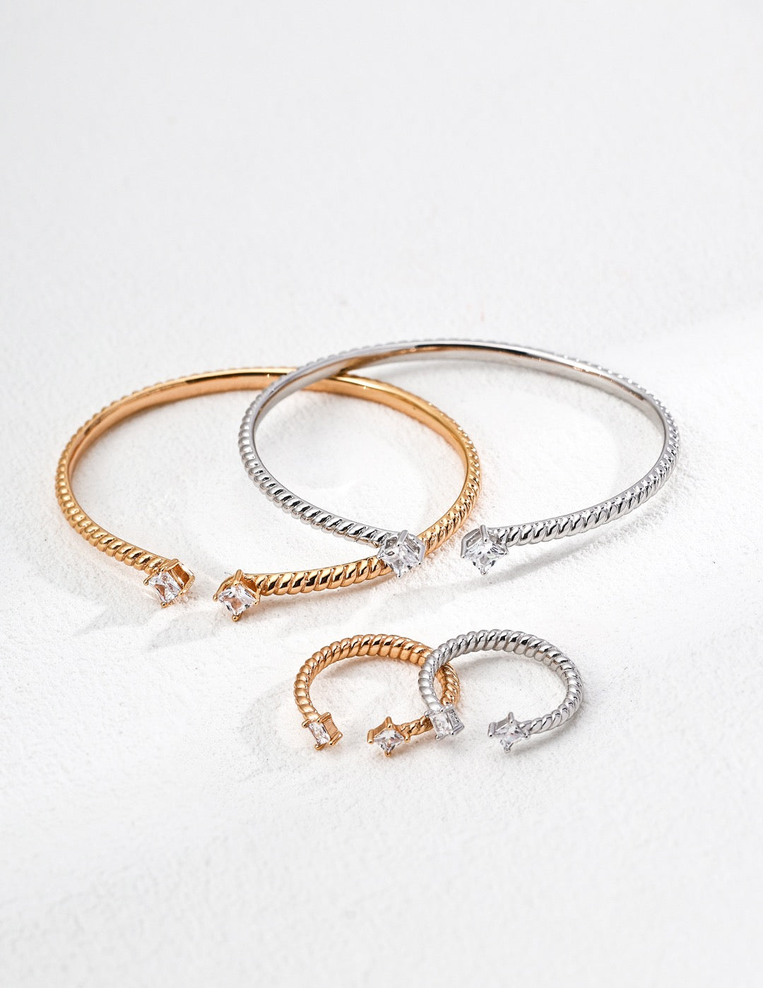 Two gold and silver bracelets on a light gray background