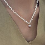 Pearl necklace with a red pendant worn by a person in a beige top.