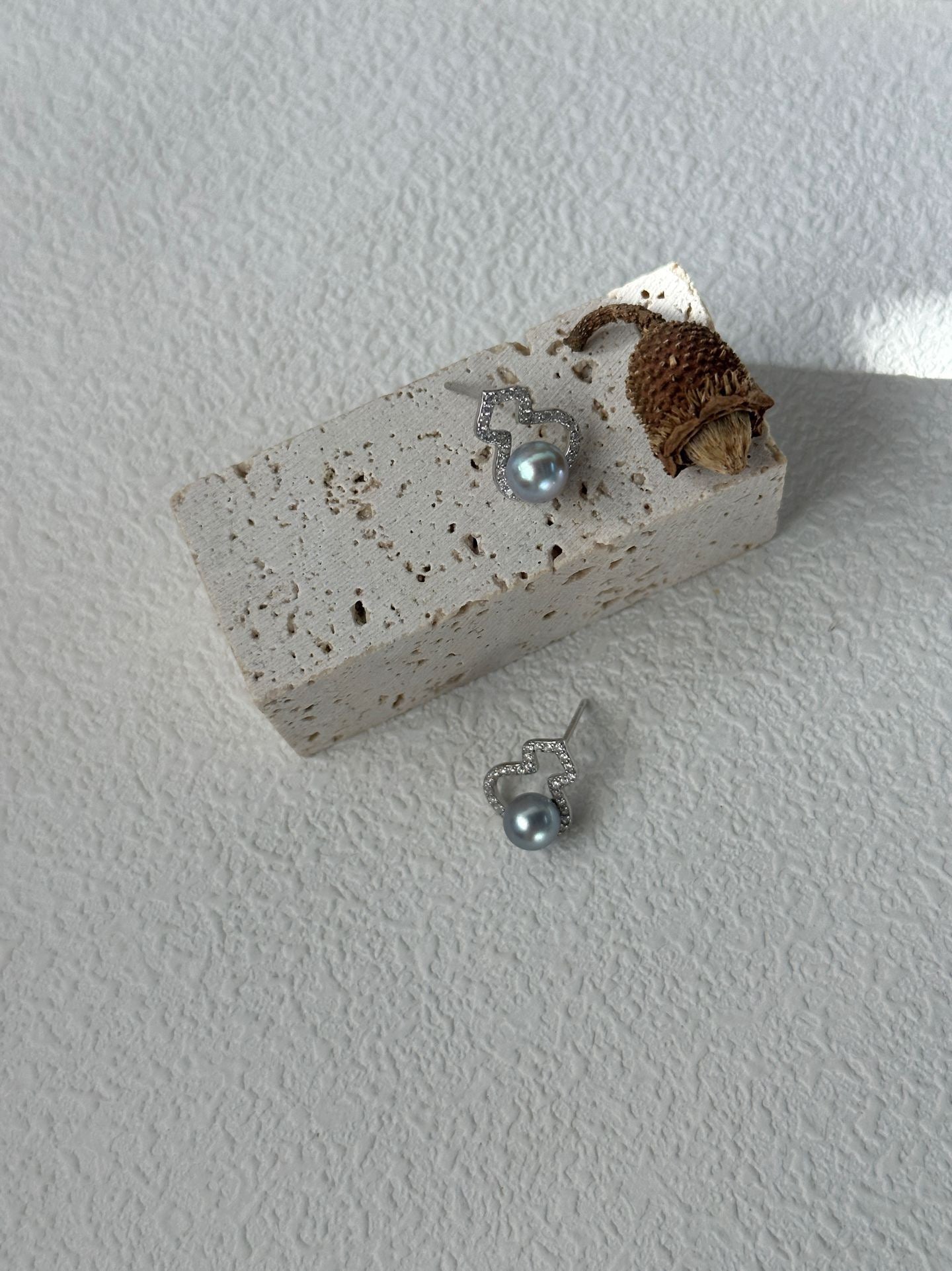 Silver earring with a small pine cone on a white surface