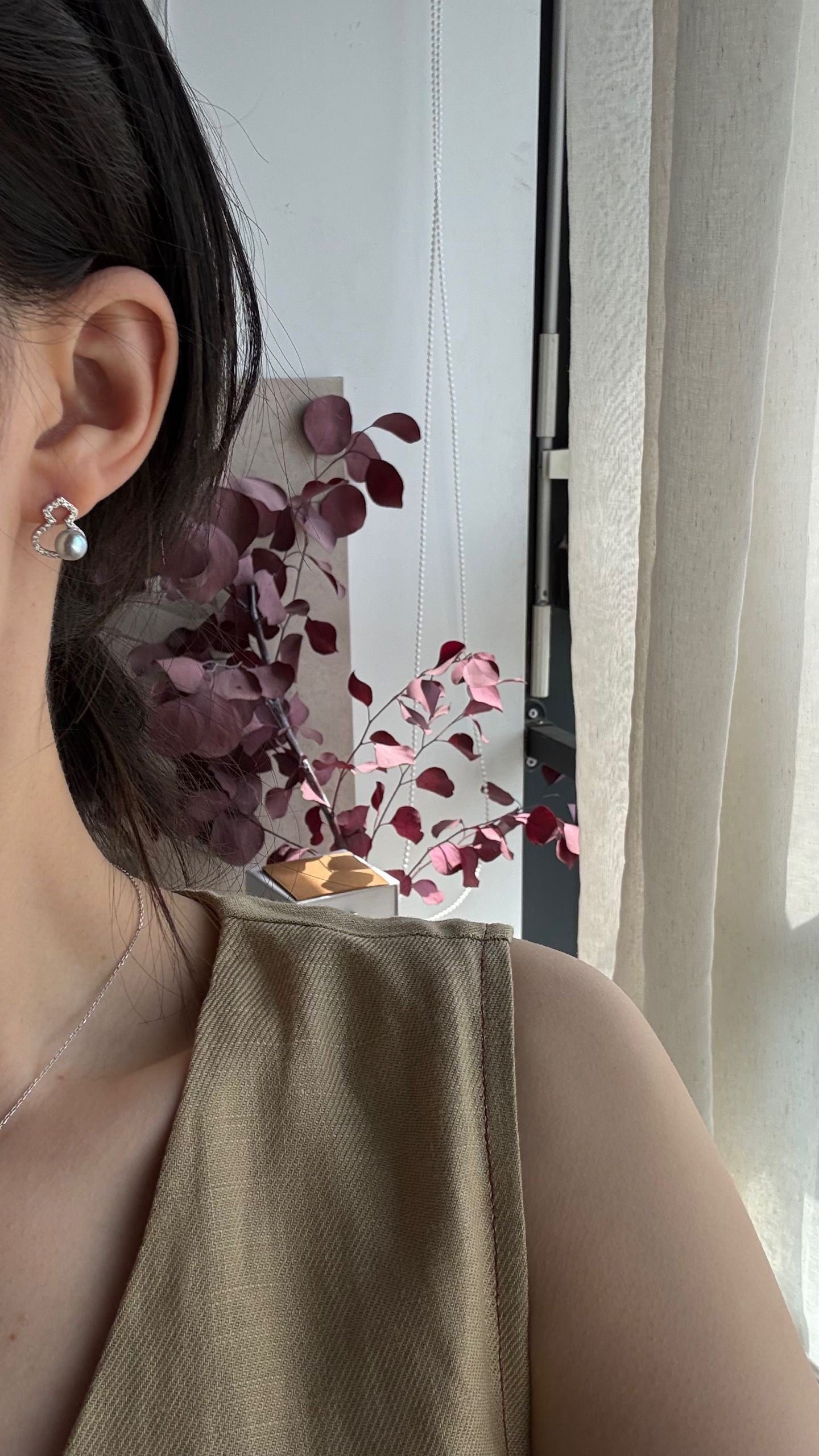 Close-up of an ear with a silver earring, wearing a beige top, with a decorative plant in the background.