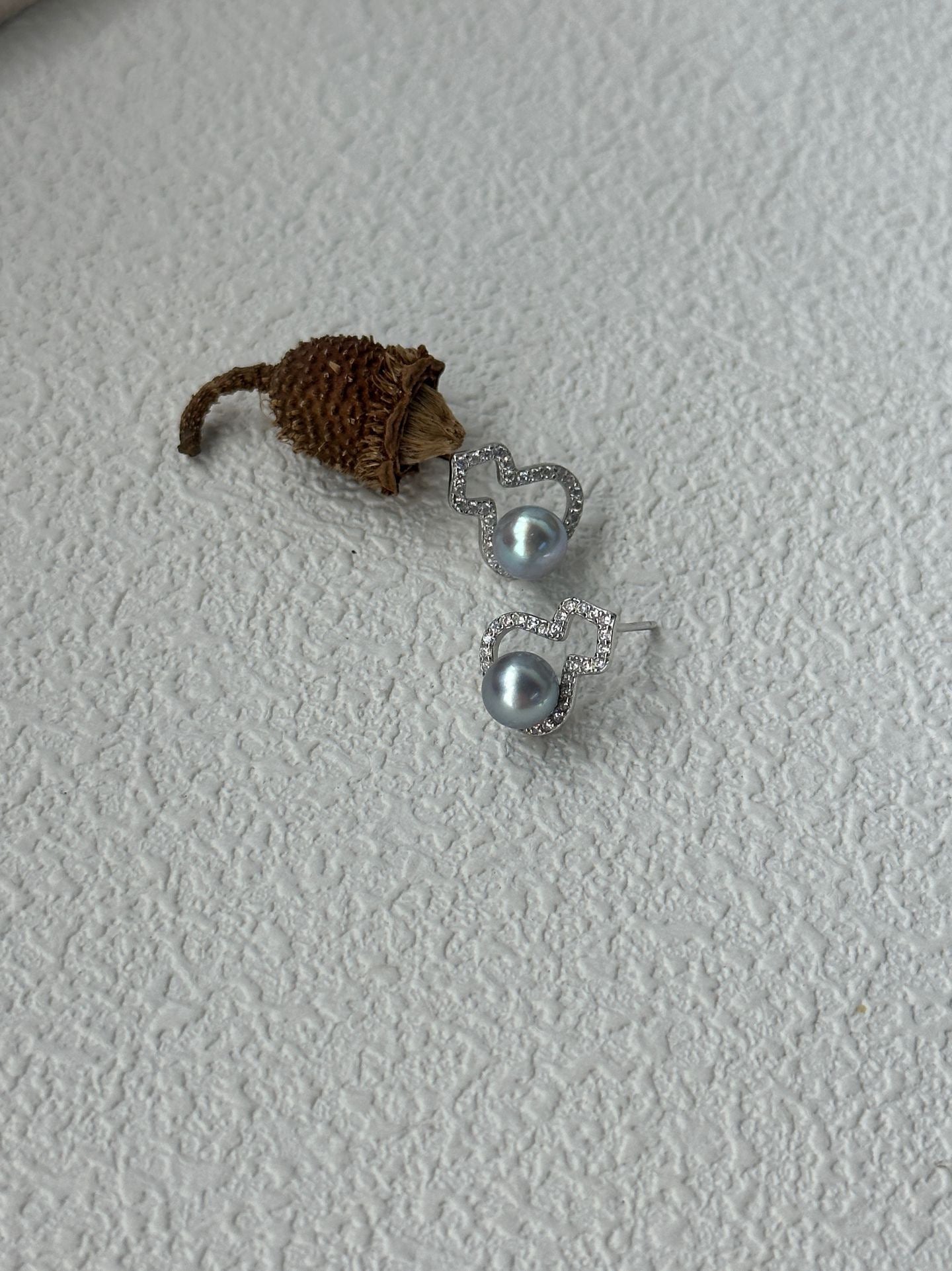 Small toy hedgehog next to a pair of silver earrings on a textured white surface