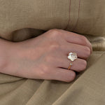 Hand wearing a ring with a clear stone on beige fabric