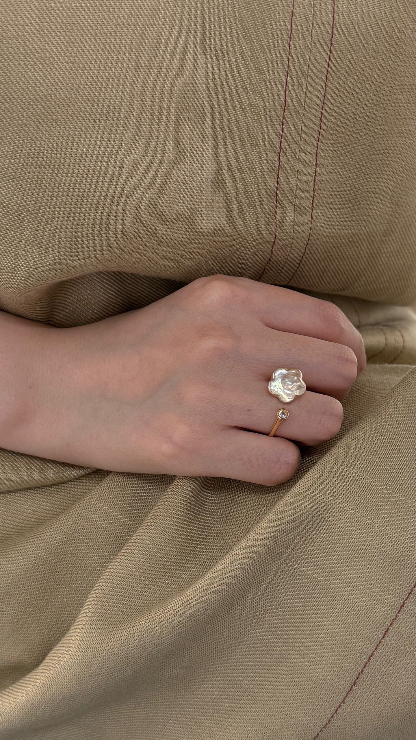 Hand wearing a ring with a clear stone on beige fabric