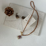 Necklace with a pendant on a white surface with a pine cone and leaves.