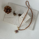 Necklace with a pendant on a white surface with a pine cone and leaves.