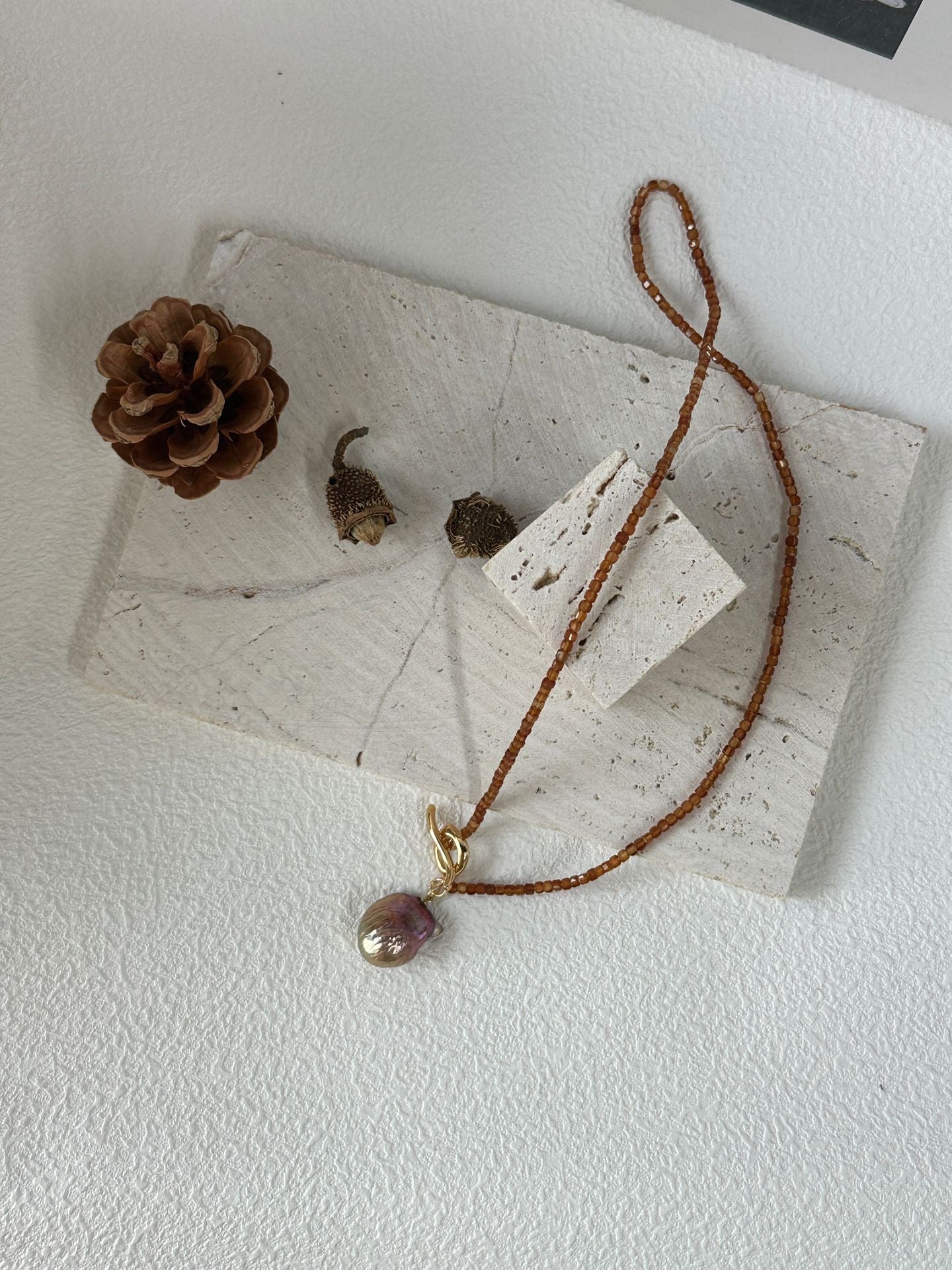 Necklace with a pendant on a white surface with a pine cone and leaves.