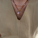 Close-up of a person wearing a pearl necklace with a pendant on a beige top.