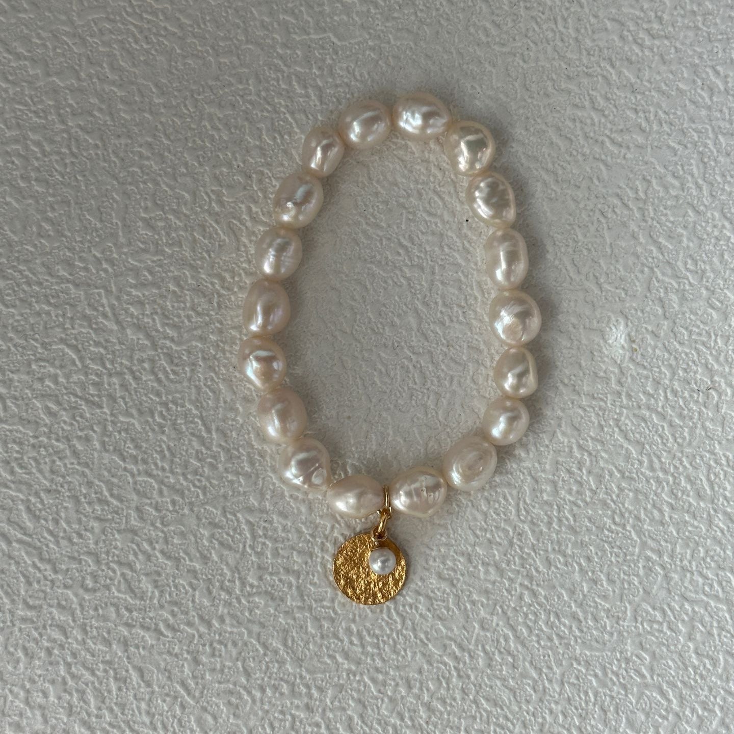 Pearl bracelet with a gold charm on a light gray background