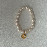 Pearl bracelet with a gold charm on a light gray background