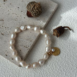 Pearl bracelet with a gold charm on a textured surface with acorns.