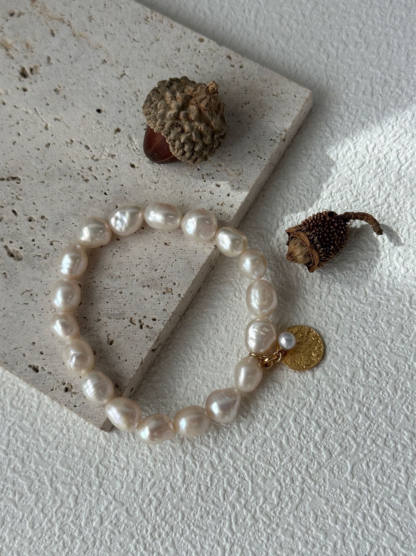 Pearl bracelet with a gold charm on a textured surface with acorns.