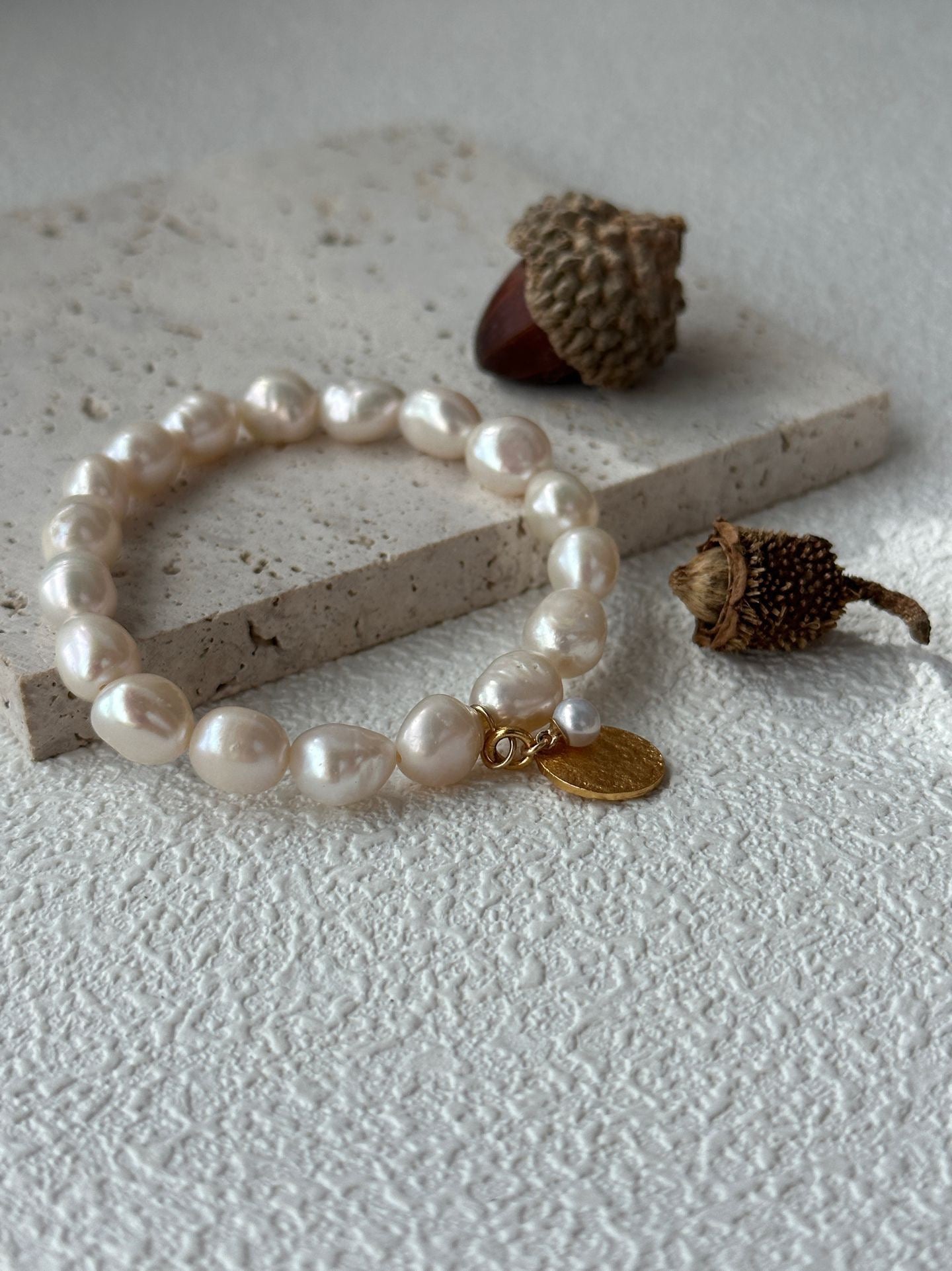 Pearl bracelet with a gold tag on a textured surface with acorns