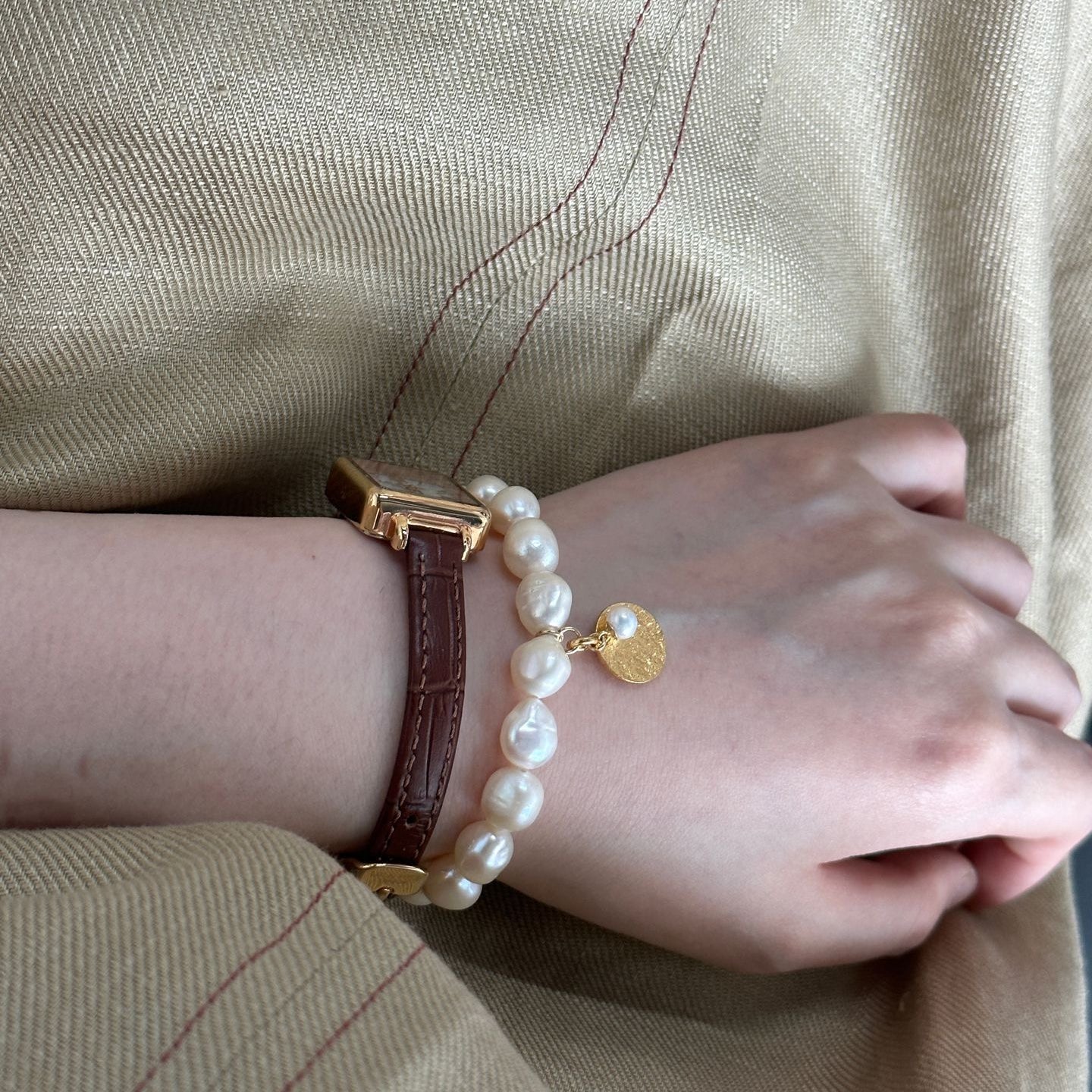 Person wearing a pearl bracelet with a gold clasp on a beige background