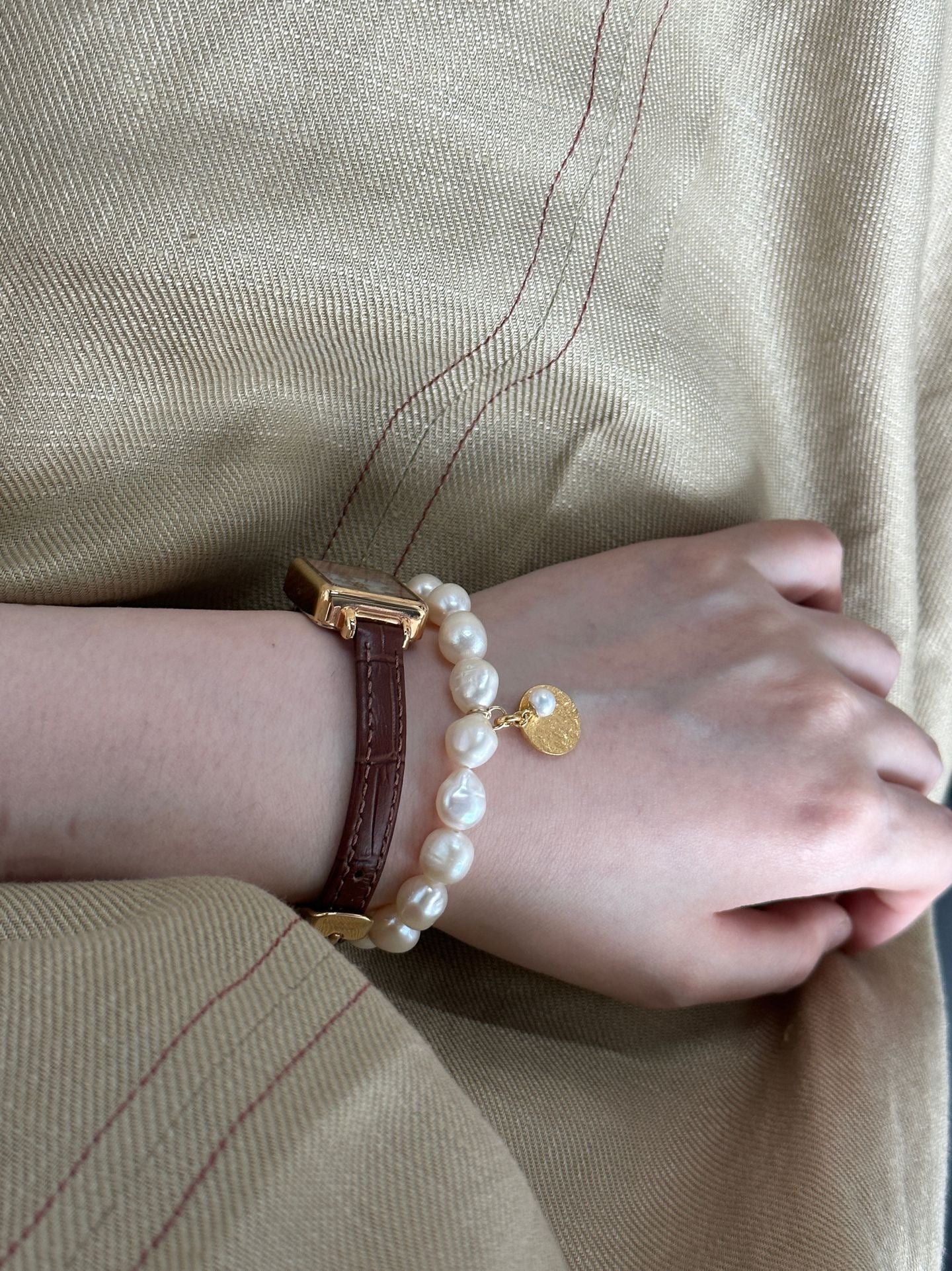 Person wearing a pearl bracelet with a gold clasp on a beige background