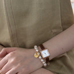 Person wearing a watch and bracelet on a beige background