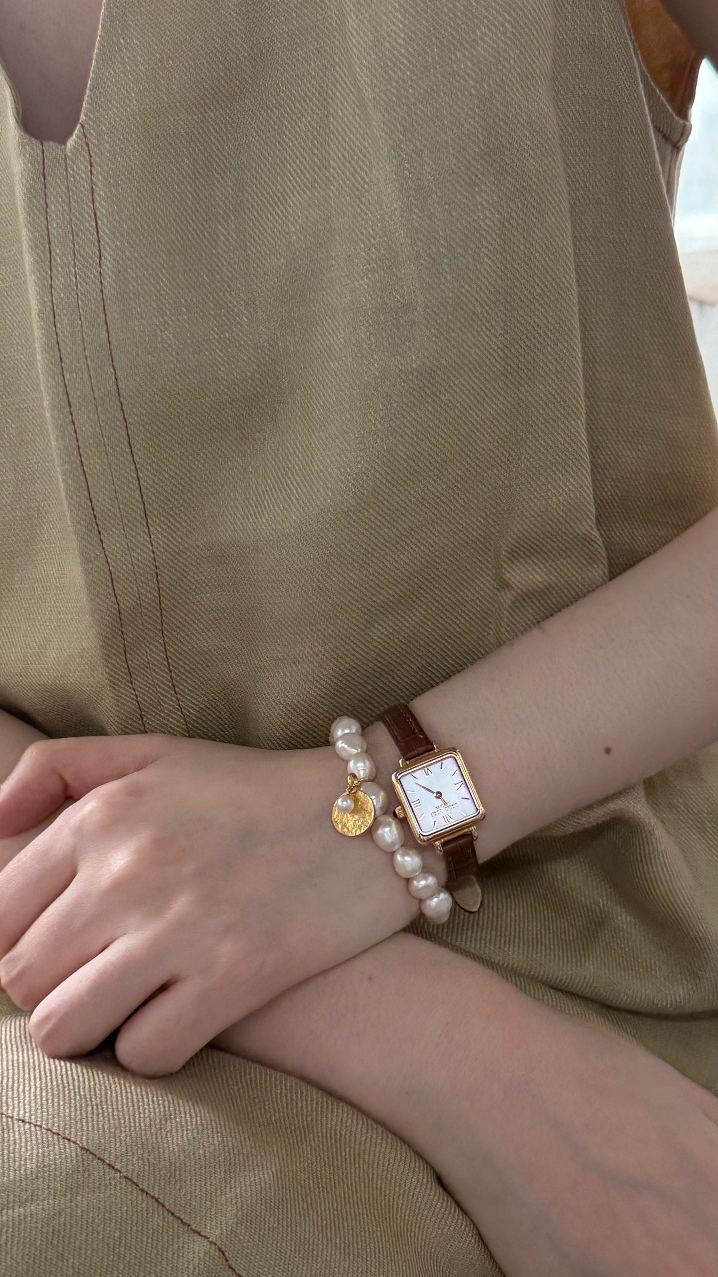 Person wearing a watch and bracelet on a beige background