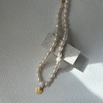 Pearl necklace with a gold clasp on a light gray background