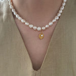 Pearl necklace with a gold pendant worn by a person in a beige outfit.
