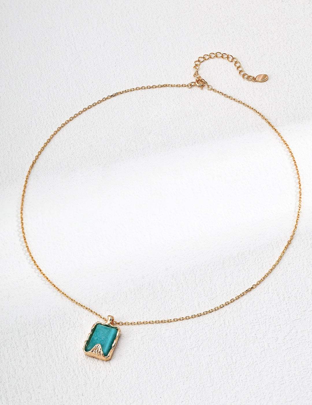 Gold necklace with a green pendant on a white background