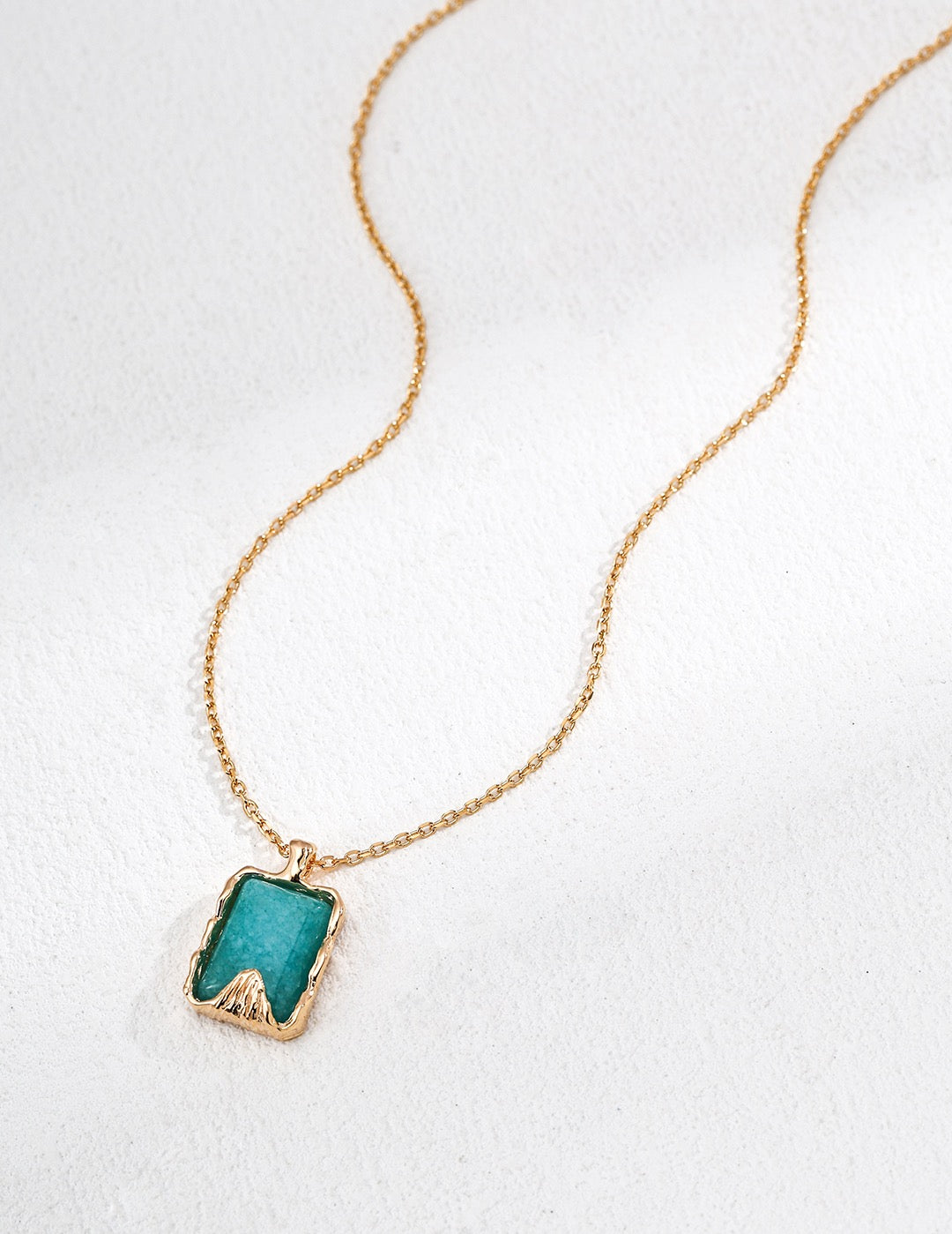 Gold necklace with a green pendant on a white background