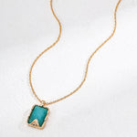 Gold necklace with a green pendant on a white background