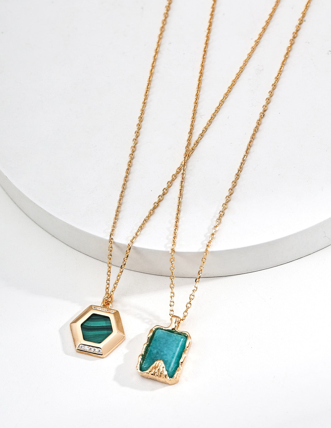 Two gold necklaces with green pendants on a white background