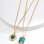 Two gold necklaces with green pendants on a white background