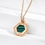 Gold necklace with a green hexagonal pendant on a white background