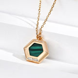 Gold necklace with a green hexagonal pendant on a white background