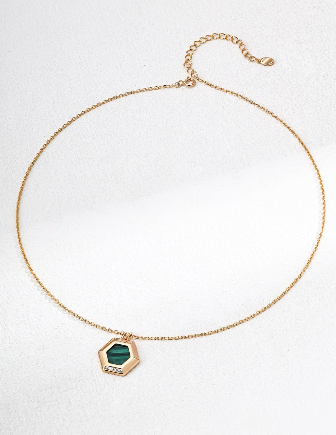 Gold necklace with a green hexagonal pendant on a white background
