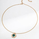 Gold necklace with a green hexagonal pendant on a white background