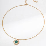 Gold necklace with a green hexagonal pendant on a white background