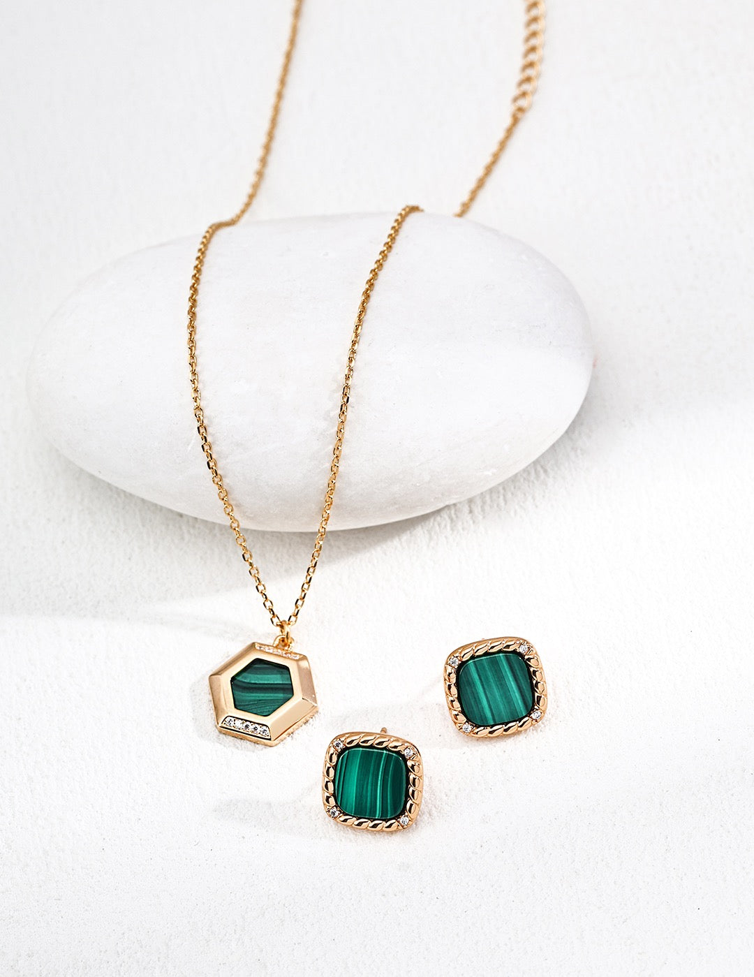 Gold necklace and earrings with green stones on a white background