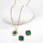 Gold necklace and earrings with green stones on a white background