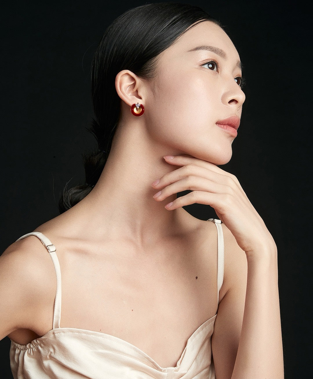 Woman wearing a gold earring against a black background
