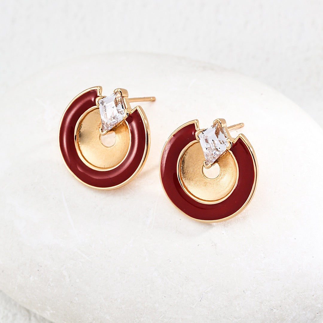 Pair of earrings with gold and red circular design on a white cushion