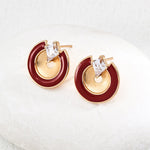Pair of earrings with gold and red circular design on a white cushion