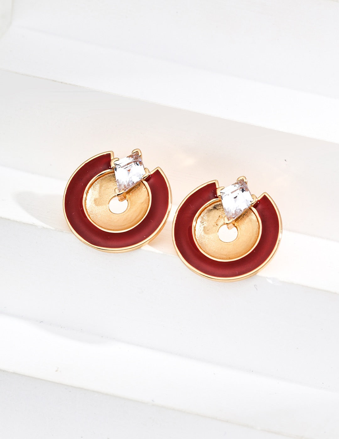 Gold and red earrings with clear gemstones on a white surface