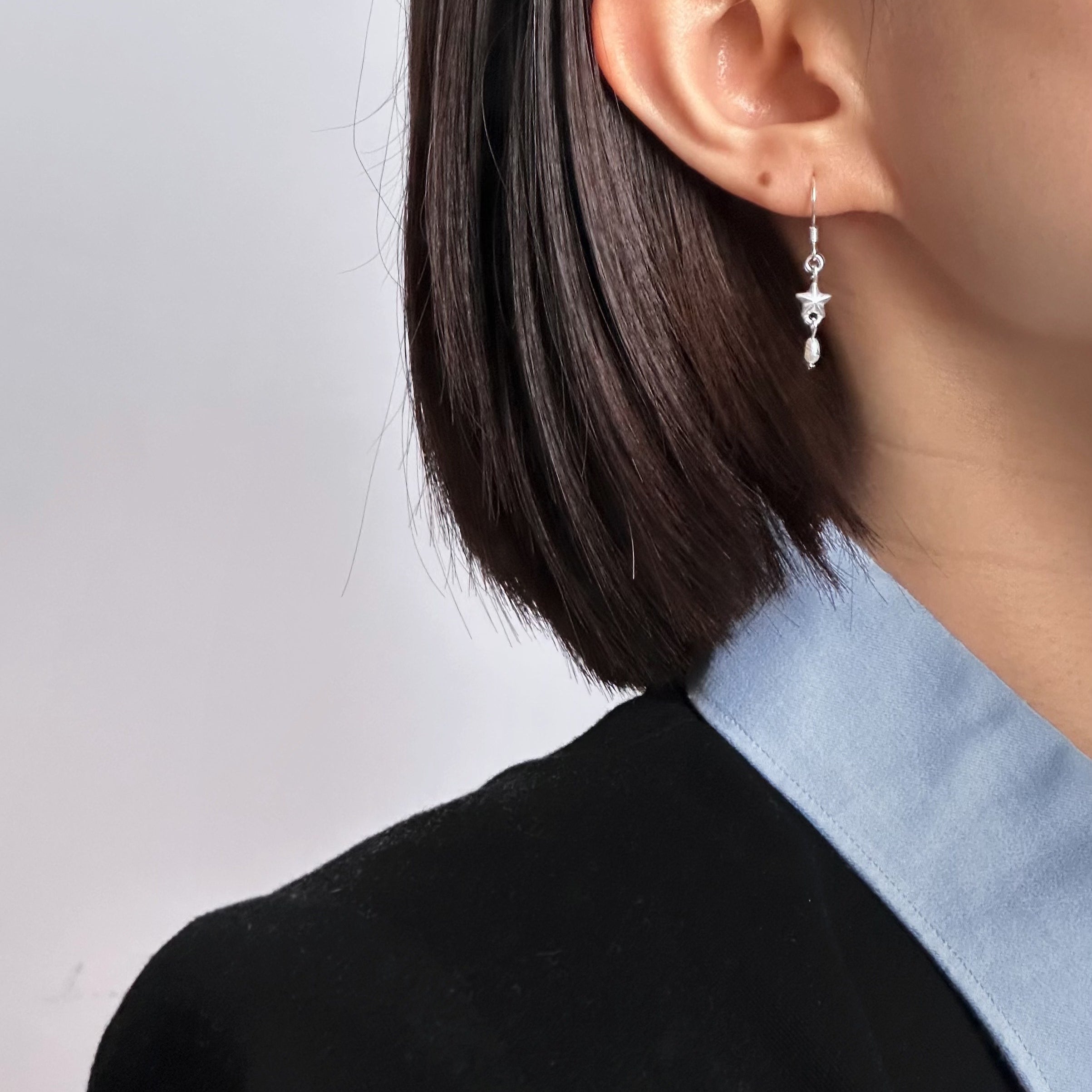 Person wearing a delicate silver earring with a clear gemstone against a neutral background