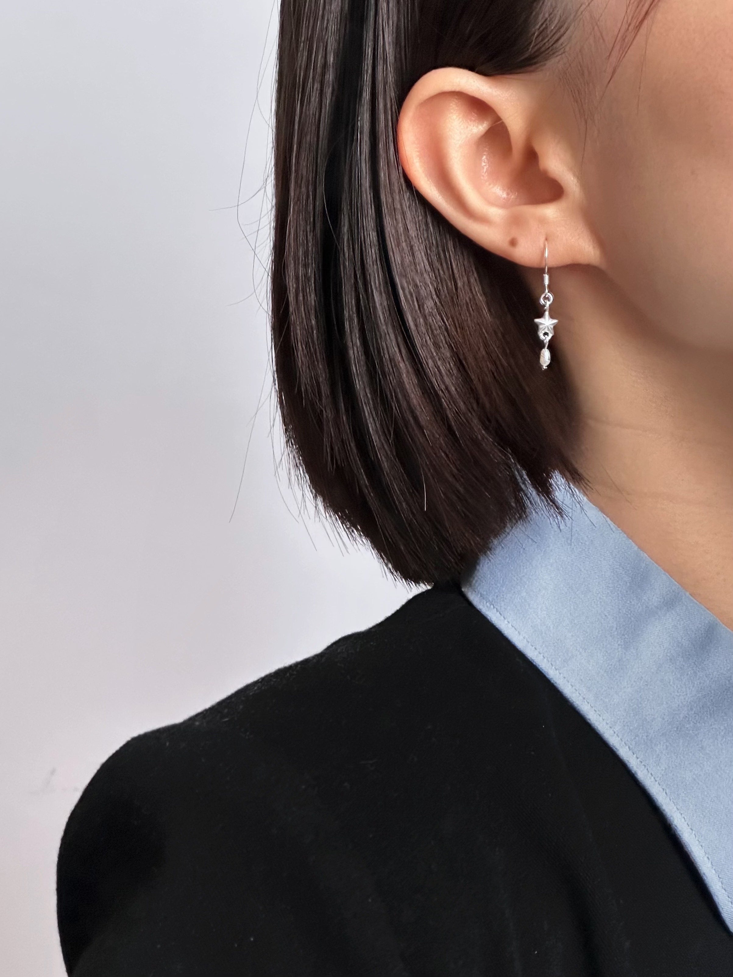 Person wearing a delicate silver earring with a clear gemstone against a neutral background